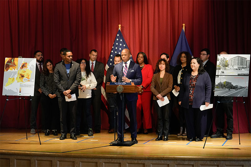 Mayor Eric Adams stands on a stage surrounded by people