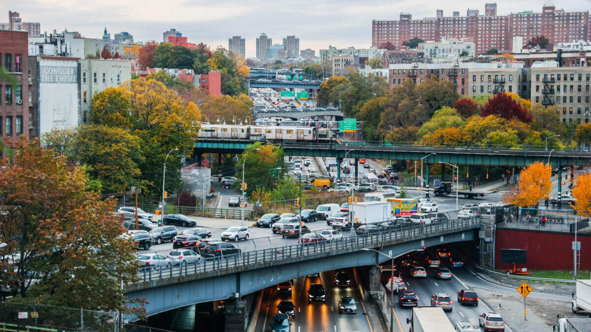 Photo from Bronx Times article of the Cross Bronx Expressway highway busy with vehicles, with an overpass with parked cars and an elevated subway