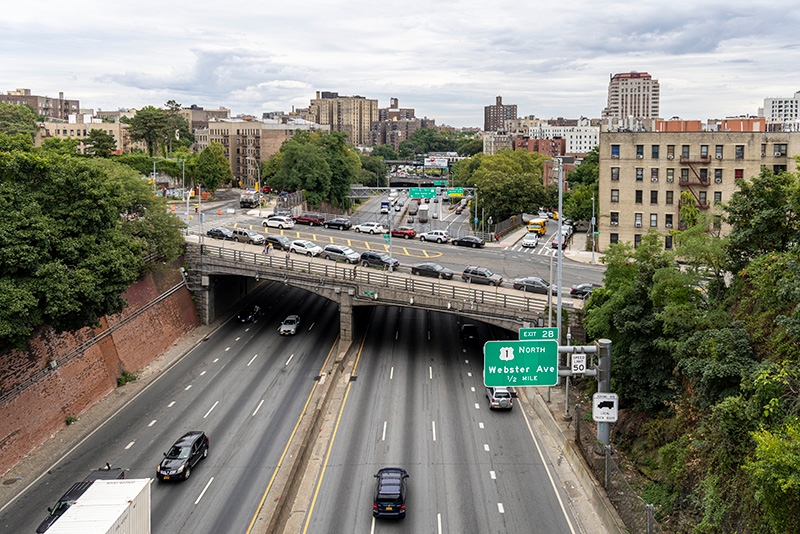 overview of an expressway with six lanes of moving vehicles and overpass with parked cars and two lanes of traffic traveling over the expressway